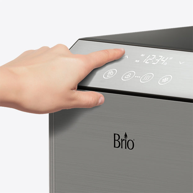 A hand touches the digital control panel of a stainless steel Brio appliance, displaying a clock and various function icons.